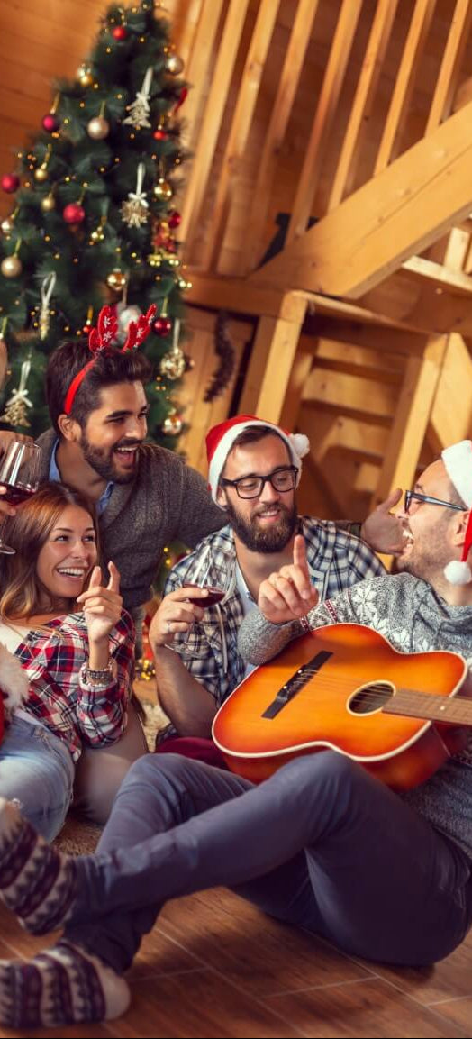 fünf Leute sitzen auf dem Boden vor einem Weihnachtsbaum und eine Person spielt Gitarre