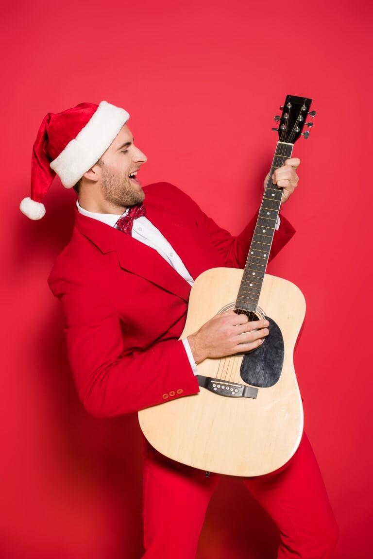 Ein Mann im roten Anzug und Nikolausmütze spielt Gitarre vor einer roten Wand