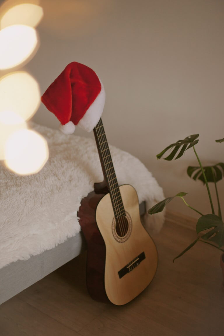 Eine Gitarre ist an einem Bett angelehnt. Auf dem Head sitzt eine Nikolausmütze