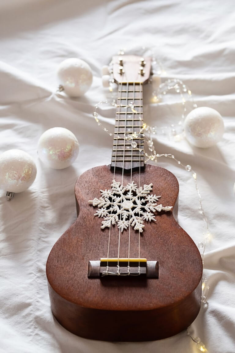 Eine braune Gitarre liegt auf einem weißen Laken. Weißer Weihnachtsschmuck liegt neben und um der Gitarre